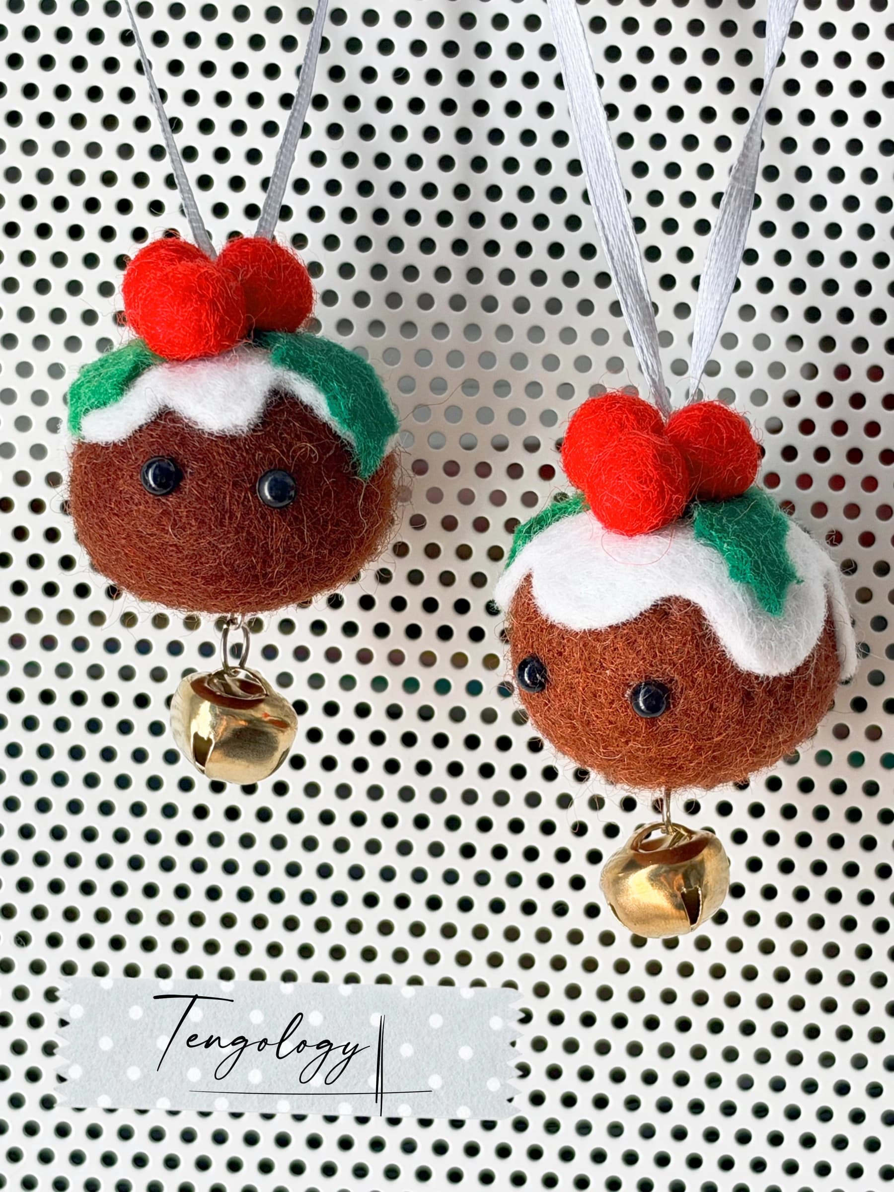 Two handmade felt Christmas pudding ornaments with bead eyes and brass bells, hanging on silver ribbons