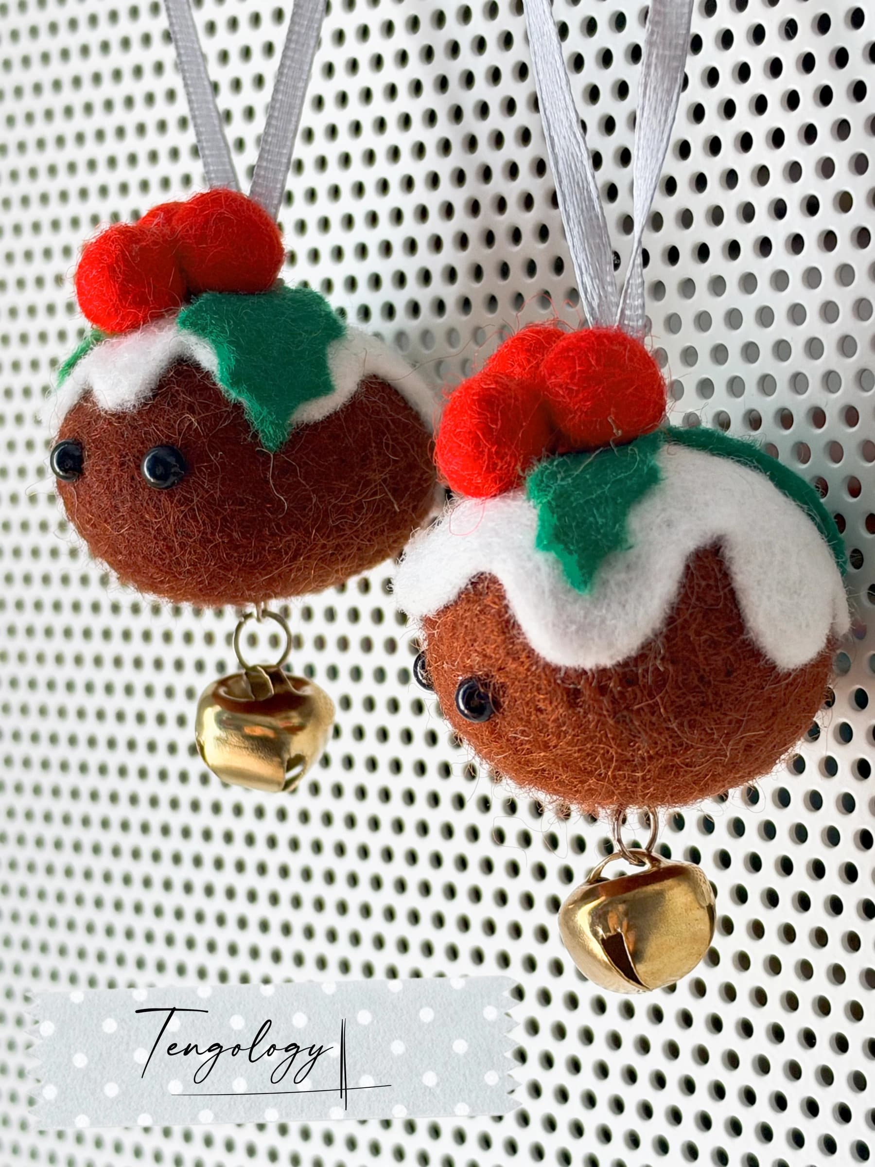 Close-up of two felt Christmas pudding ornaments, showing the needle-felted wool, felt holly and brass bells