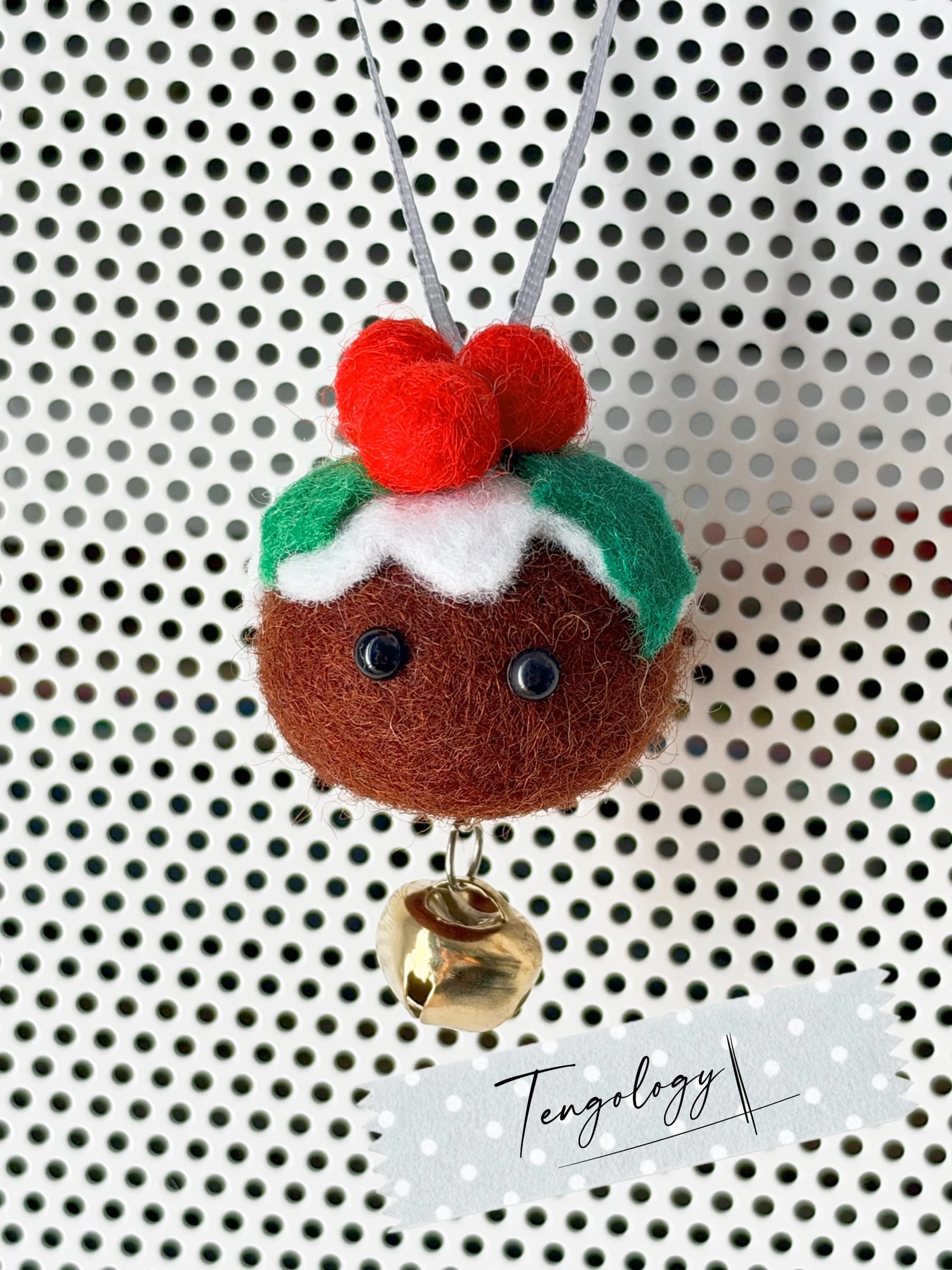 Handmade felt Christmas pudding ornament with white custard, holly leaves, three red berries and bead eyes, hanging on a silver ribbon with a brass bell