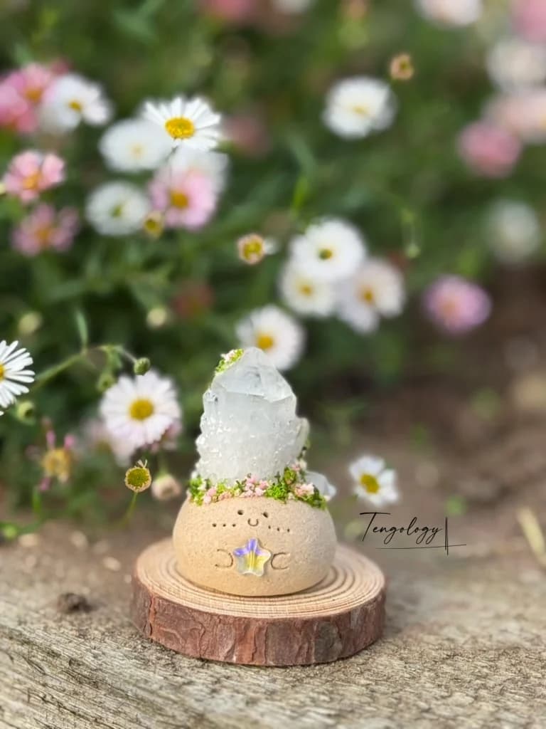 A clear quartz Crysprout on a wood slice among garden daisies
